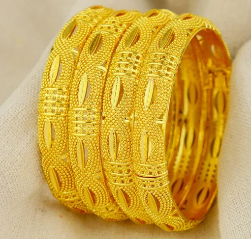 Two gold bangles with intricate designs on a beige fabric background