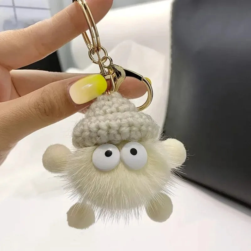Plush keychain with googly eyes held by a hand against a neutral background