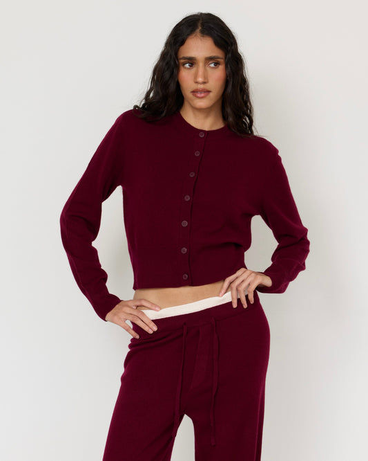 Woman modeling a luxurious burgundy cashmere cardigan with button-front closure and matching burgundy pants, elegant women’s knitwear outfit on white background