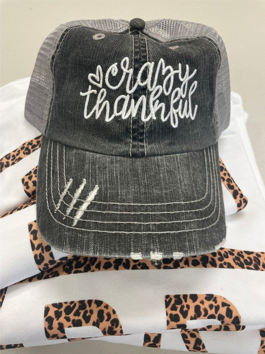 Gray distressed cap with 'Crazy Thankful' text on a leopard print surface. Vintage Distressed "Crazy Thankful" Embroidered Trucker Hat – Adjustable Unisex Mesh Baseball Cap for Thanksgiving, Fall & Everyday Wear