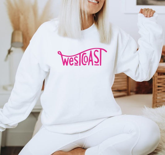 Person wearing a white sweatshirt with 'west coast' in pink text, sitting indoors.