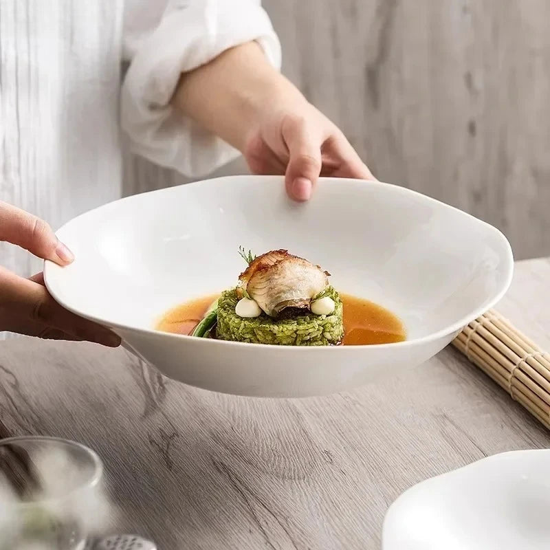Person holding a white bowl with a dish of food on a wooden table