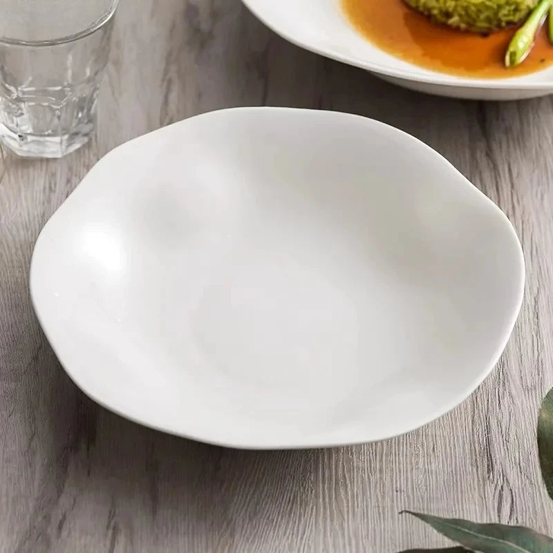 White ceramic plate on a wooden table with a glass of water and another dish in the background.