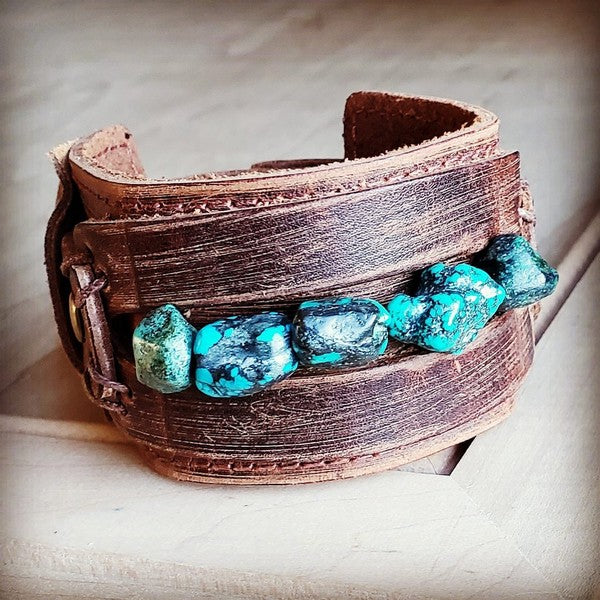 Wide Cuff with African Turquoise Chunks Wrap your wrist in natural beauty with a wide, handcrafted cuff that features a genuine strand of chunky African turquoise. The distressed leather finish adds earthy depth, while the stone brings that bold green-blue glow. Every cuff is hand-created—meaning your piece will be uniquely yours, with its own mix of turquoise shades and matrix patterns.