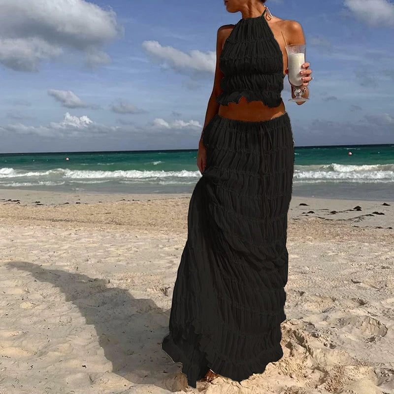Woman in a black halter top and long skirt standing on a beach with ocean view.
