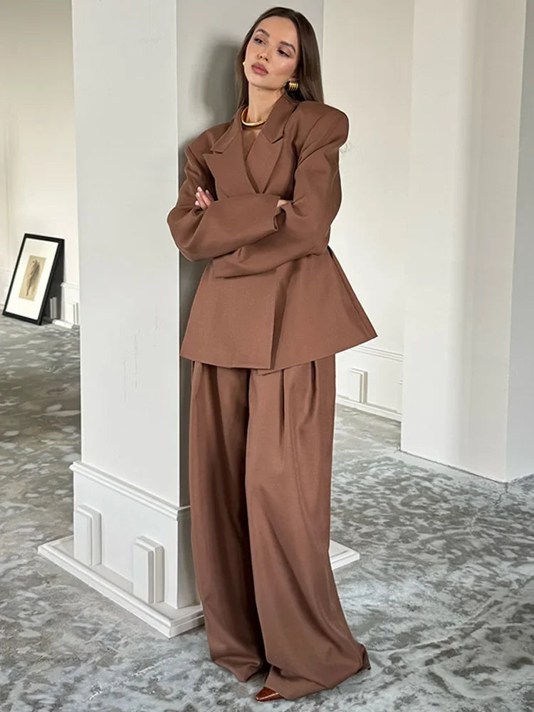 Woman in a brown suit standing in a room with a mirror and framed picture. Woman in a brown outfit standing on a street with a building in the background oversized blazer business suit for women chic business suit