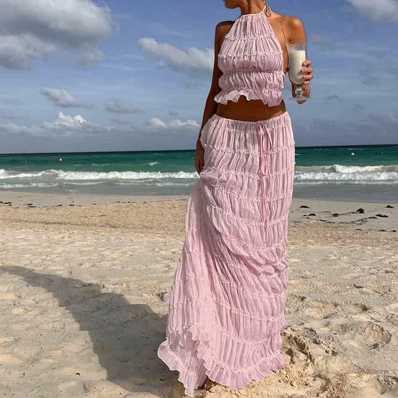 Woman in a pink 2 piece skirt and top beach standing on a beach with ocean in the background