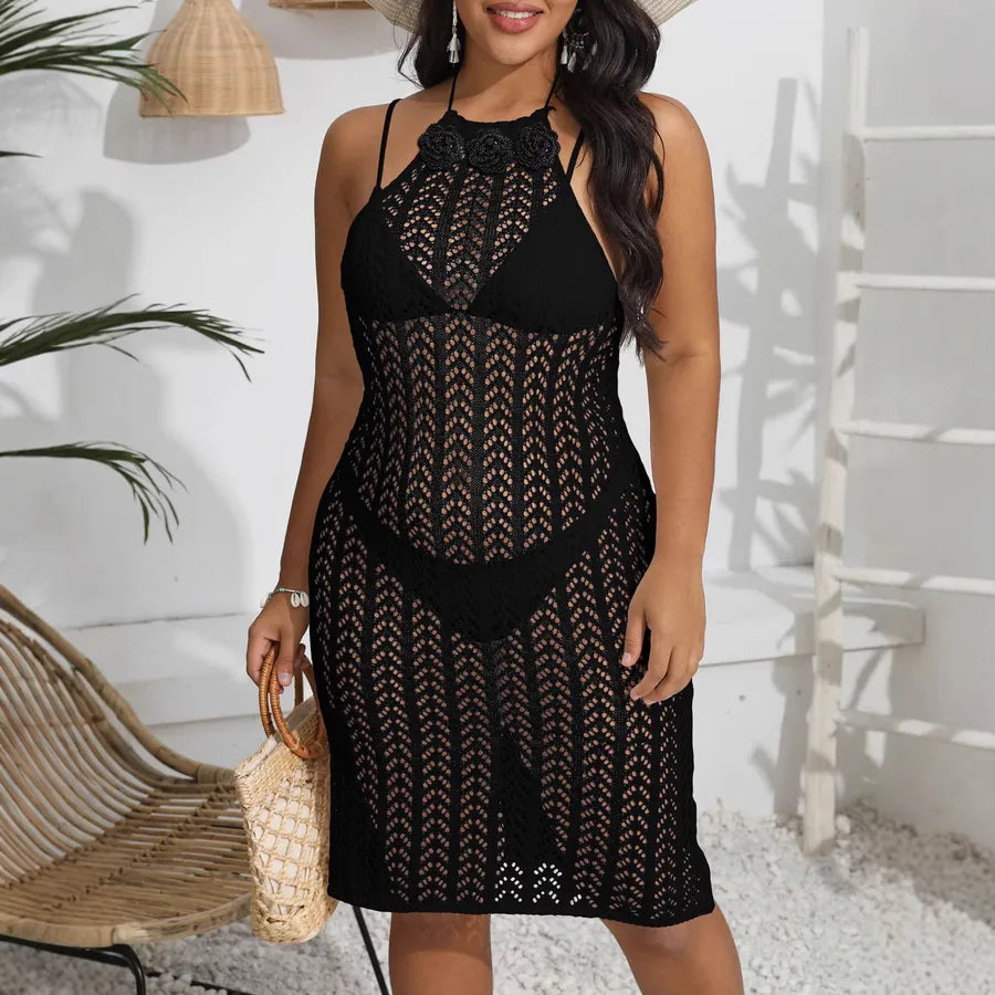 Woman wearing a black lace dress standing outdoors with a white wall and plant in the background.