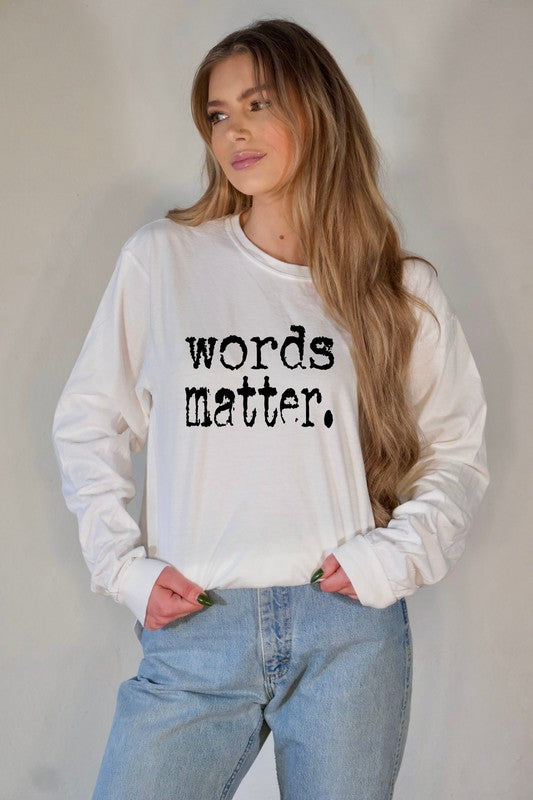 Woman modeling a white long sleeve graphic tee with the phrase "words matter." in distressed black lettering, paired with light wash jeans against a neutral backdrop.