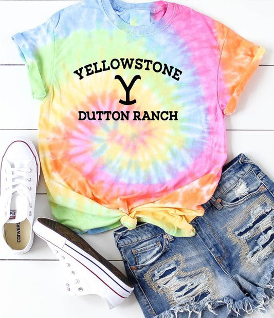Tie-dye t-shirt with 'Yellowstone Dutton Ranch' text, paired with denim shorts and white sneakers on a wooden floor.