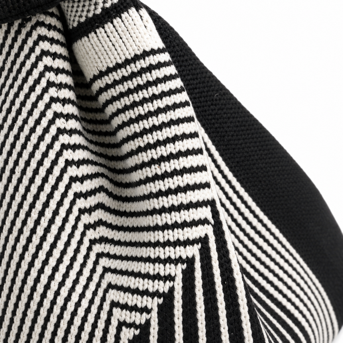 Close-up of a black and off-white knit textile with a geometric zigzag pattern and a solid black ribbed section, shown against a white background.