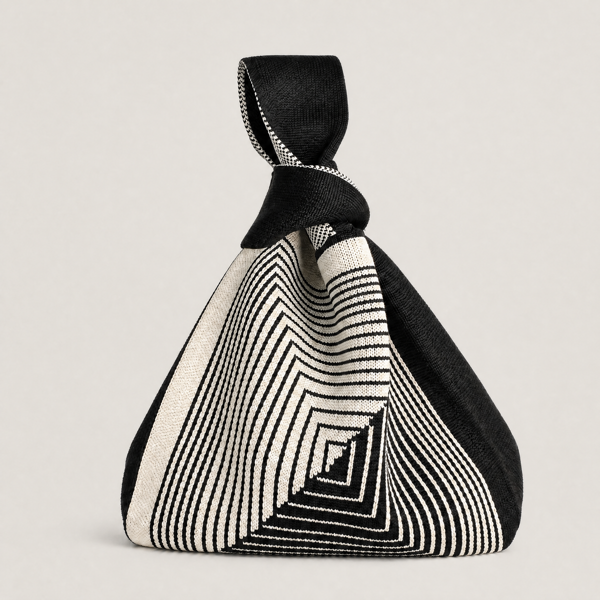 A black and off-white geometric patterned bag with a knotted top handle, shown against a neutral light gray background.