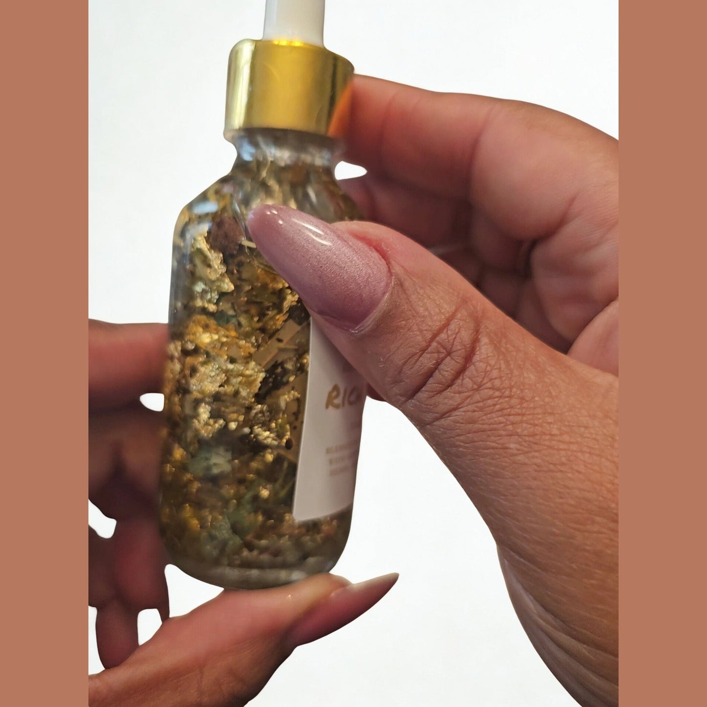 Hand holding a glass dropper bottle with a gold cap against a white background. Rich Bitch Money Drawing Hoodoo Conjure Oil | Money Attraction Oil | Wealth Ritual Oil | Prosperity Rootwork Oil | Abundance Spiritual Supply