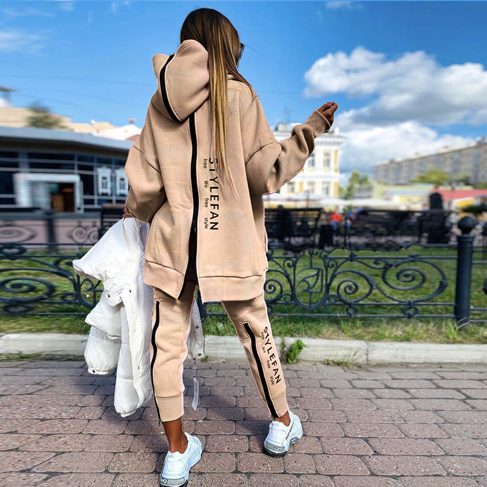 Person wearing a beige zip up back tracksuit with 'STYLEFAN' text, standing on a street with buildings and greenery in the background