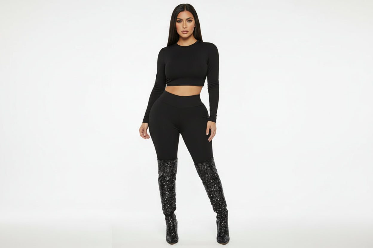 Woman wearing a black long-sleeve top and leggings with sparkly black boots on a white background