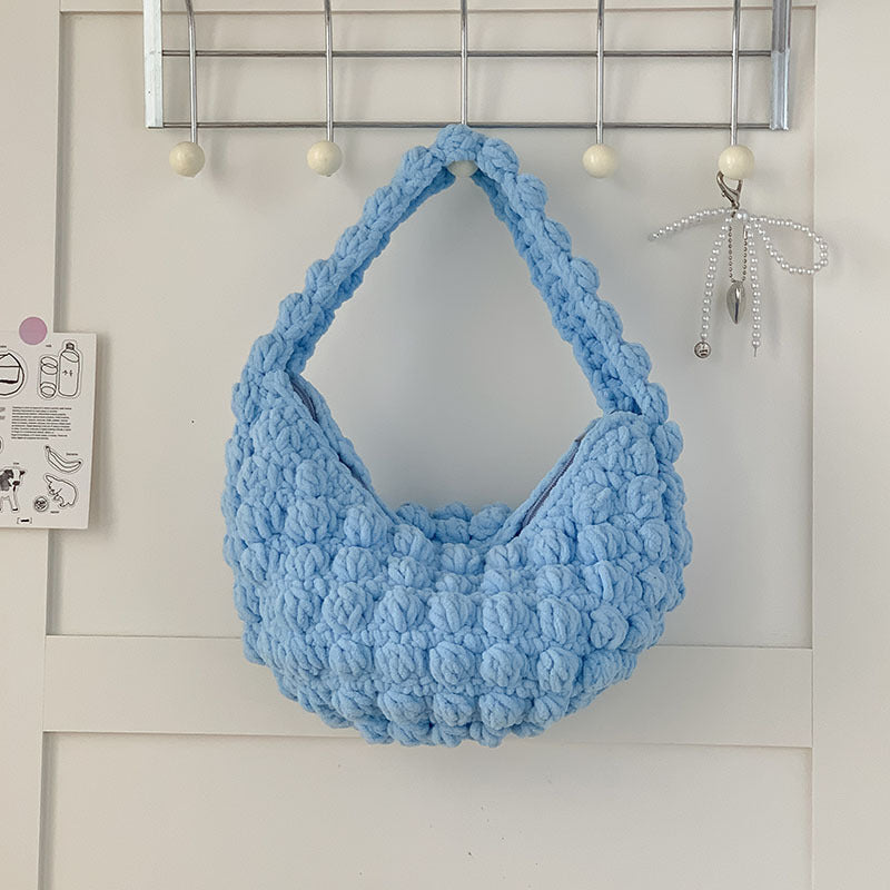 Blue textured handbag hanging on a white door with hooks.