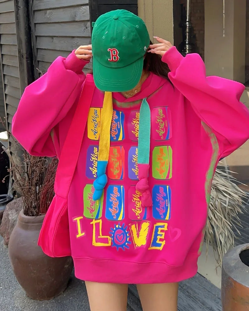Person wearing a bright pink hoodie with colorful text and a green cap outdoors.