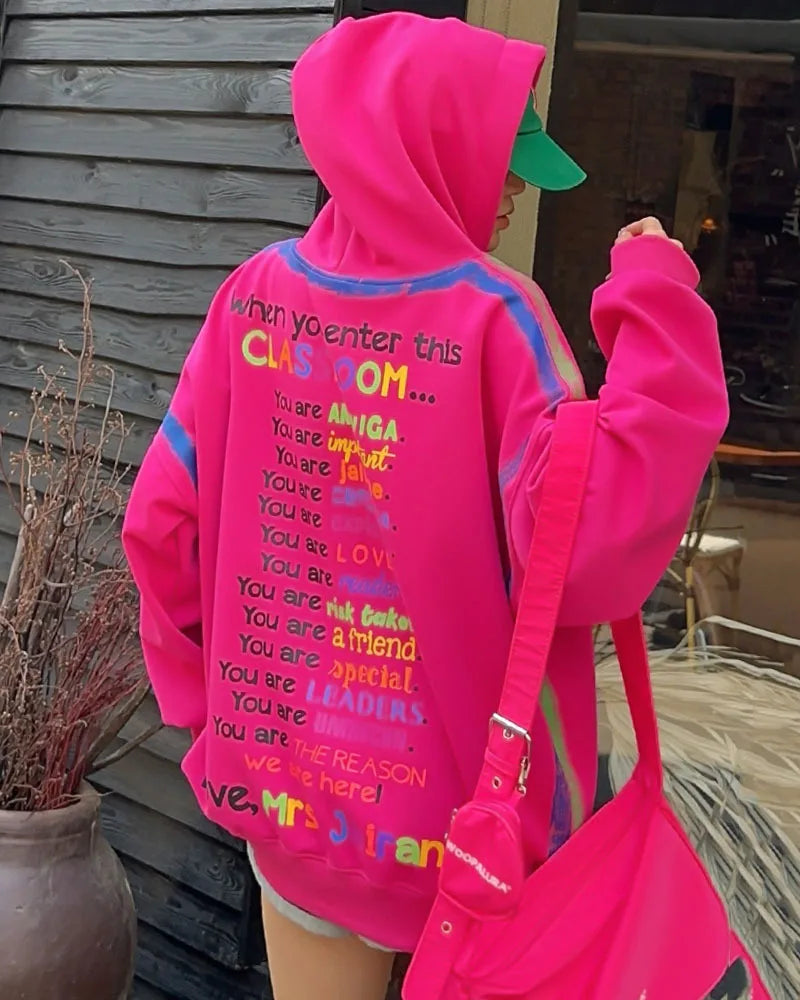 Person wearing a bright pink hoodie with colorful text outdoors.
