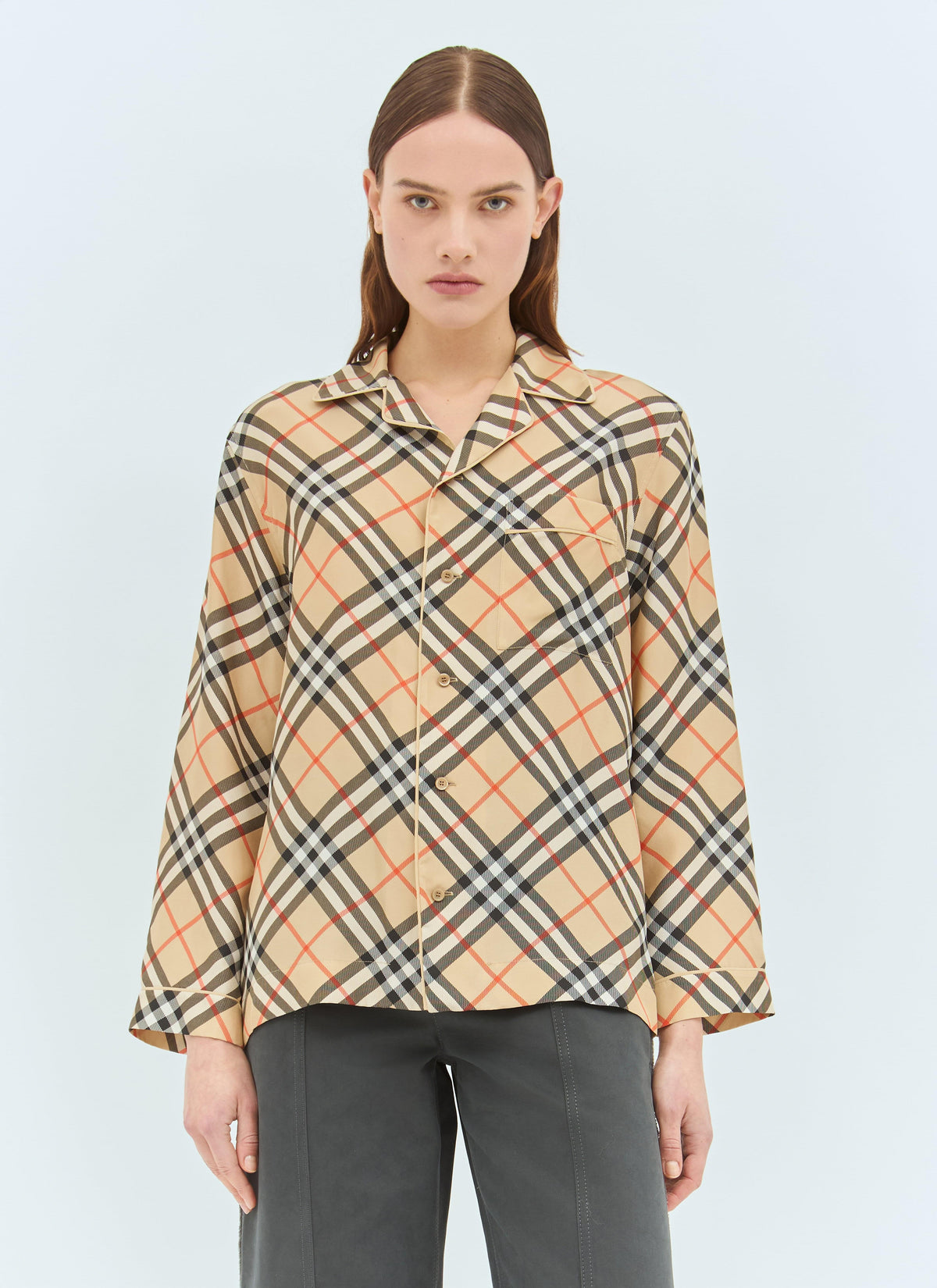 Model wearing a luxury Burberry check silk pyjama shirt with a revere collar, front button fastening, and long sleeves, captured against a clean, light blue studio background.