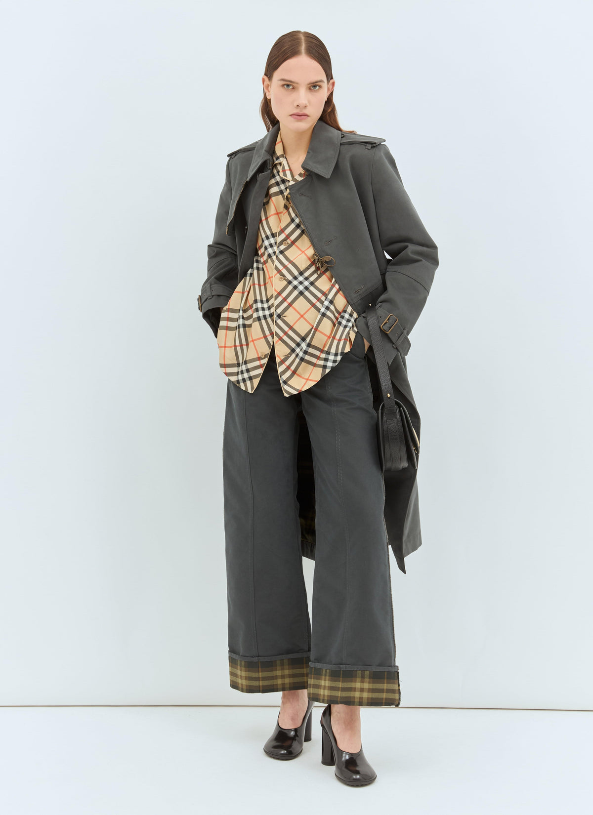 Model wearing a stylish Burberry silk pyjama shirt featuring the brand's iconic check print, styled with matching trousers and a dark grey coat against a minimalist light blue background.