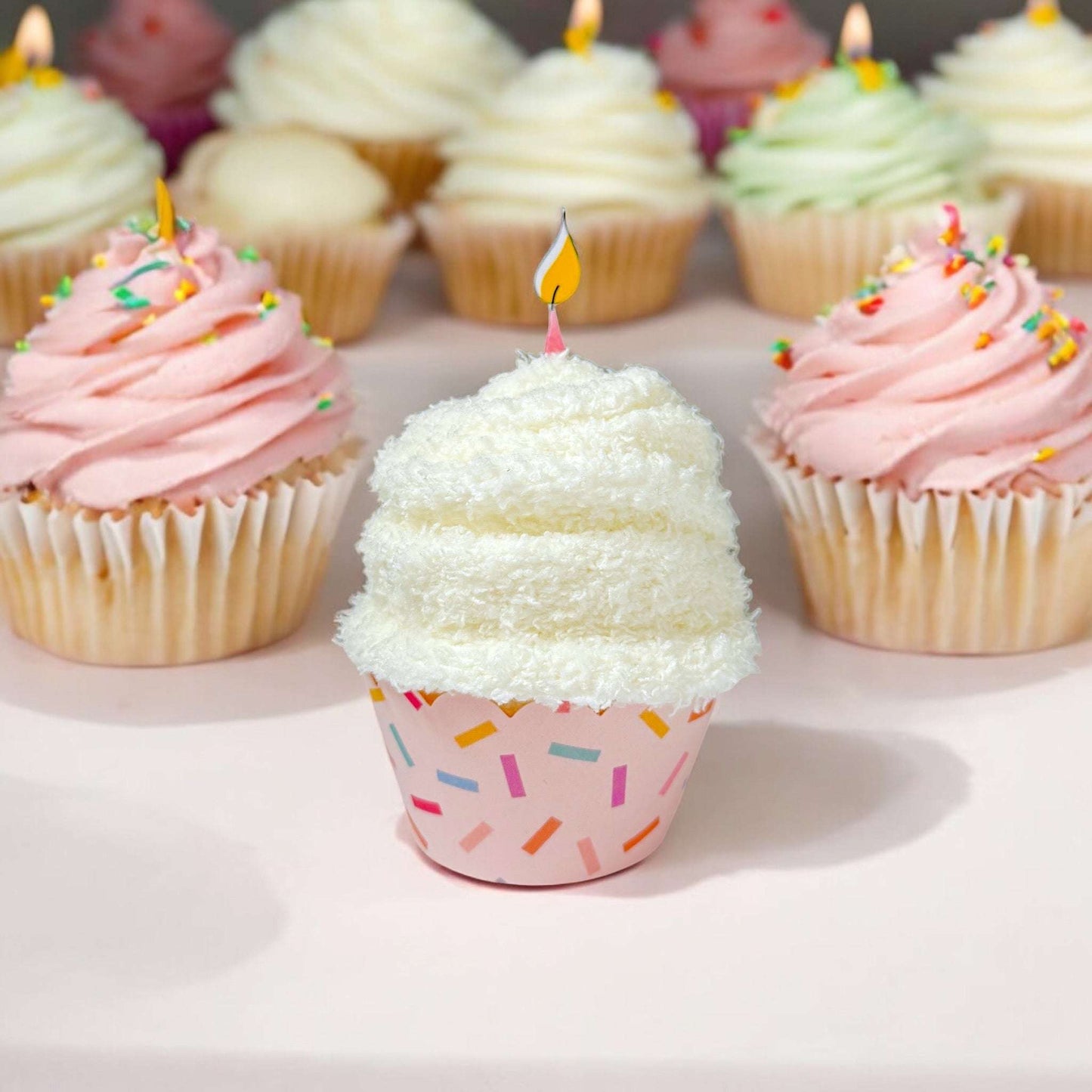 Cupcakes with pink and white frosting, sprinkles, and candles on a light background