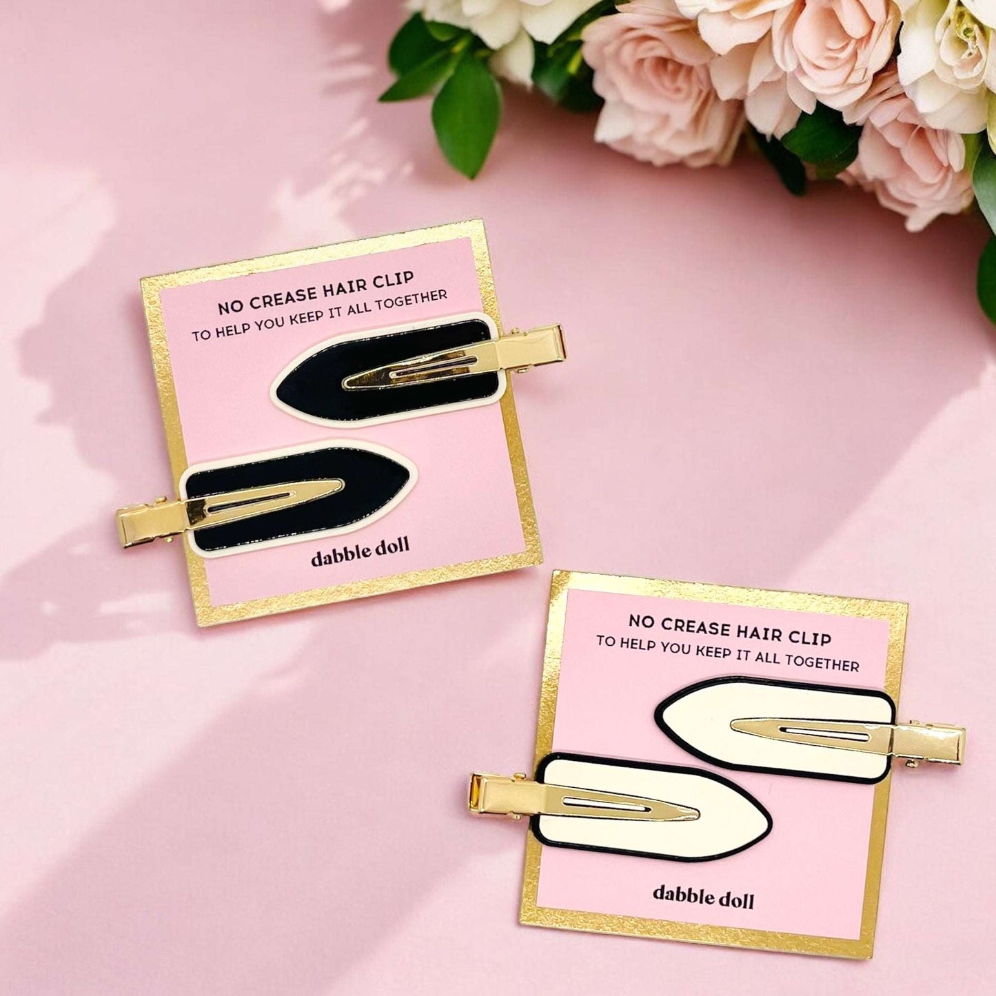 Two hair clip packages with black and gold hair clips on a pink background with flowers.