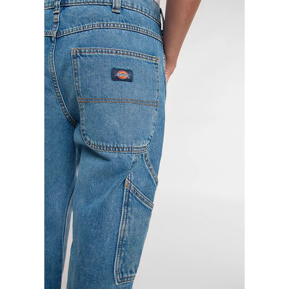 Blue jeans with a Dickies logo on the pocket against a white background