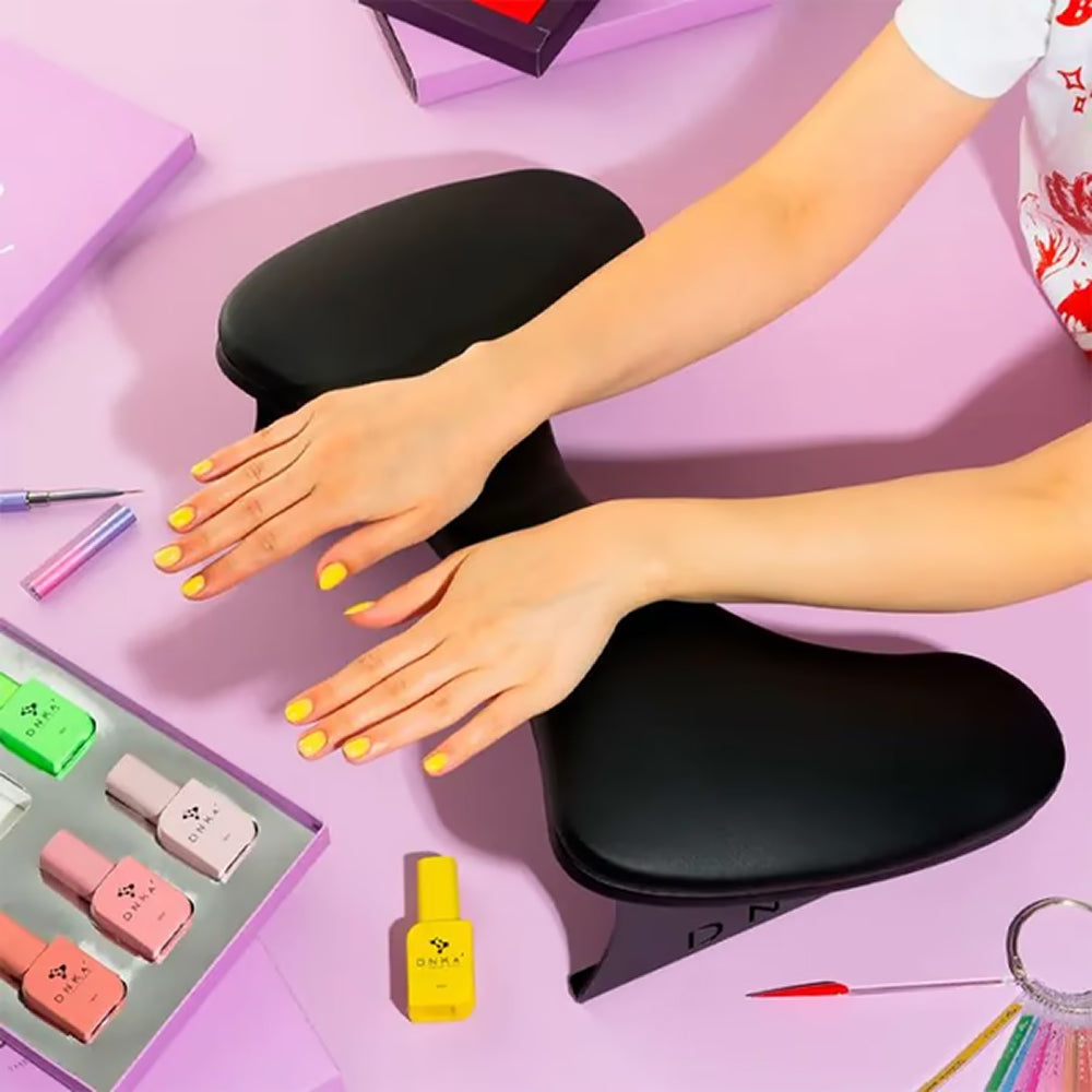 Anatomical black armrest for manicure set on a pink desk, featuring professional nail polish bottles and manicure tools arranged nearby for a comfortable salon session.