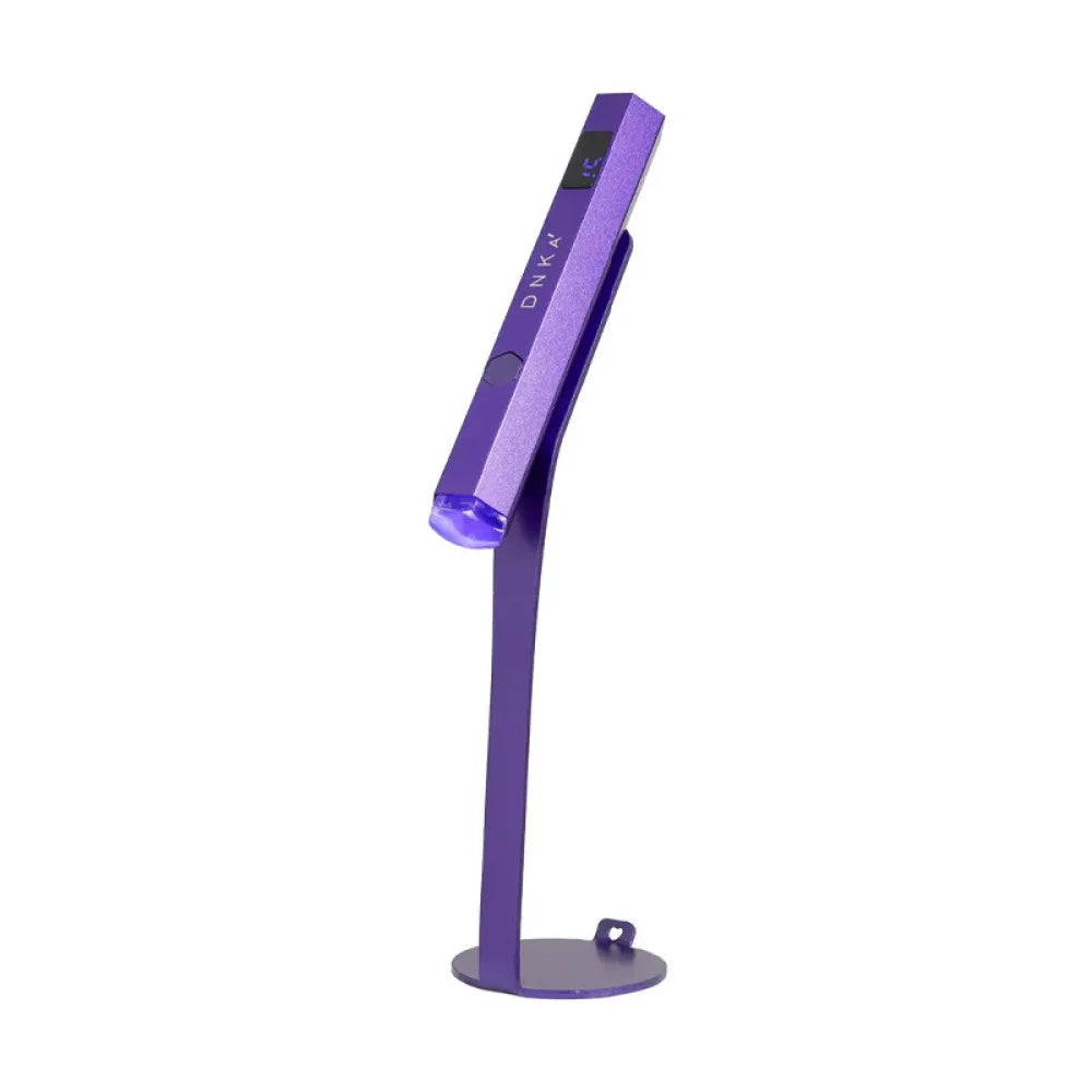 Compact, rechargeable DNKa Lumos Light UV/LED flashlight in purple, shown mounted on its magnetic stand against a clean white background.
