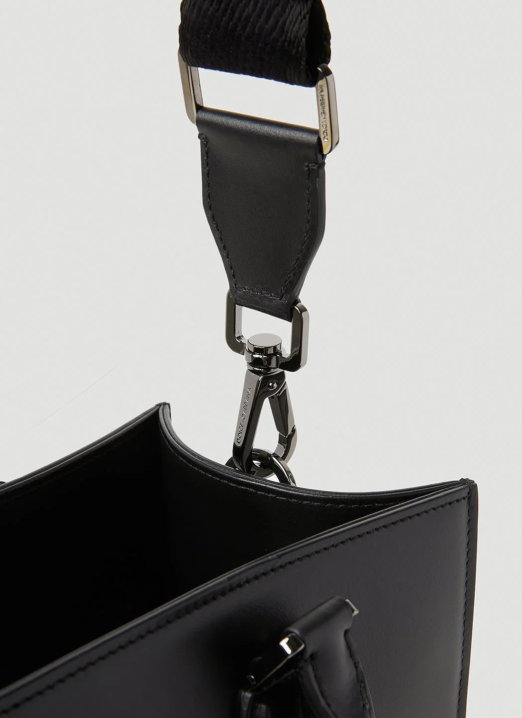 Close-up of a black handbag with a shoulder strap on a light gray background