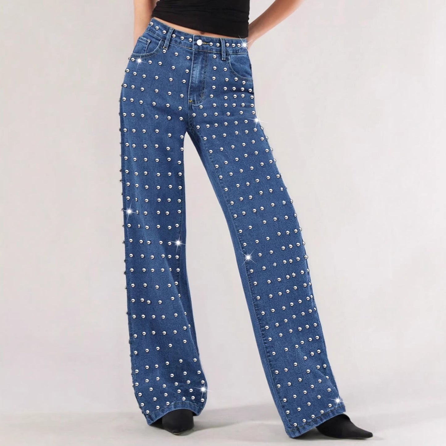 Blue wide-leg denim jeans covered in silver rhinestones, modeled against a light gray studio background.