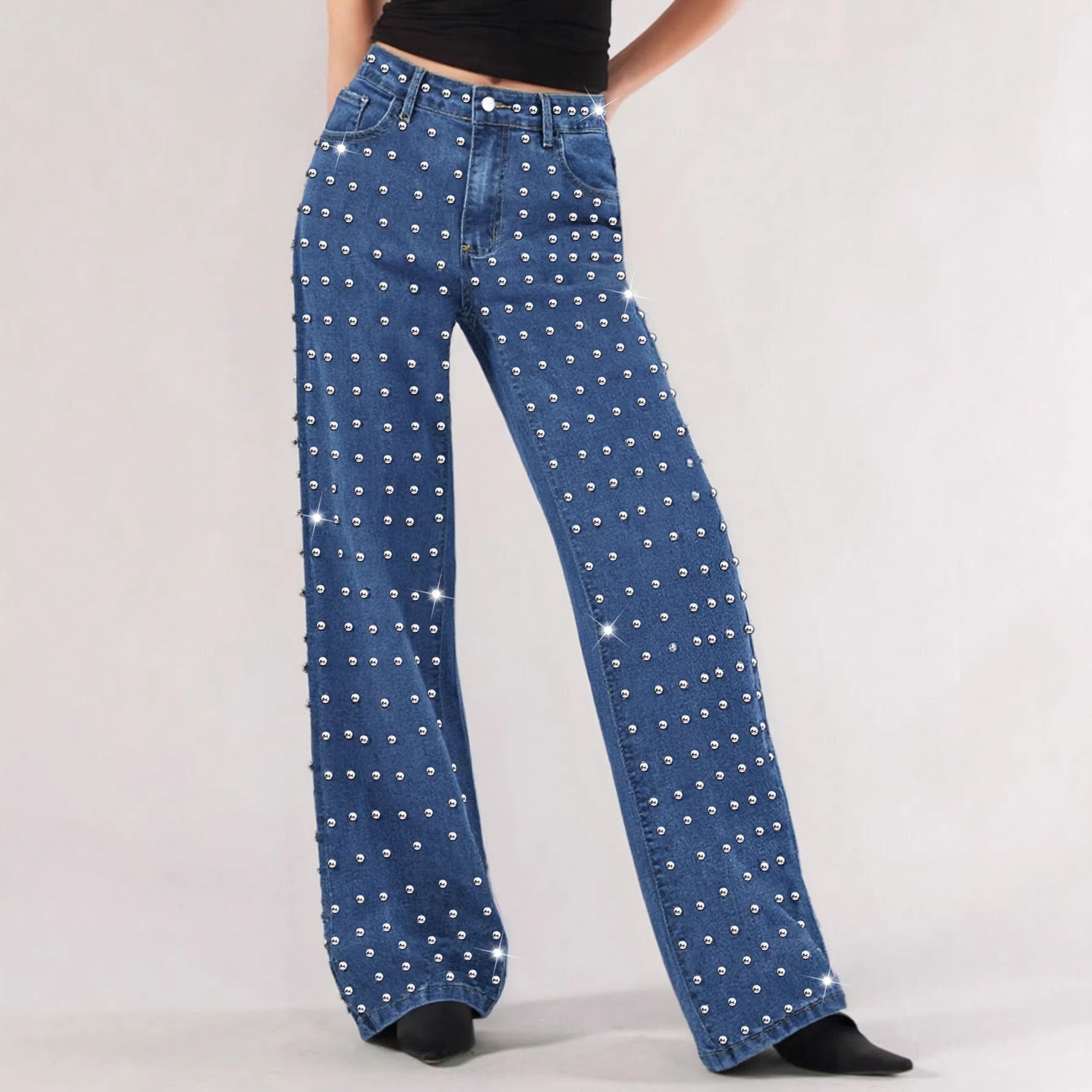 Blue wide-leg denim jeans covered in silver rhinestones, modeled against a light gray studio background.