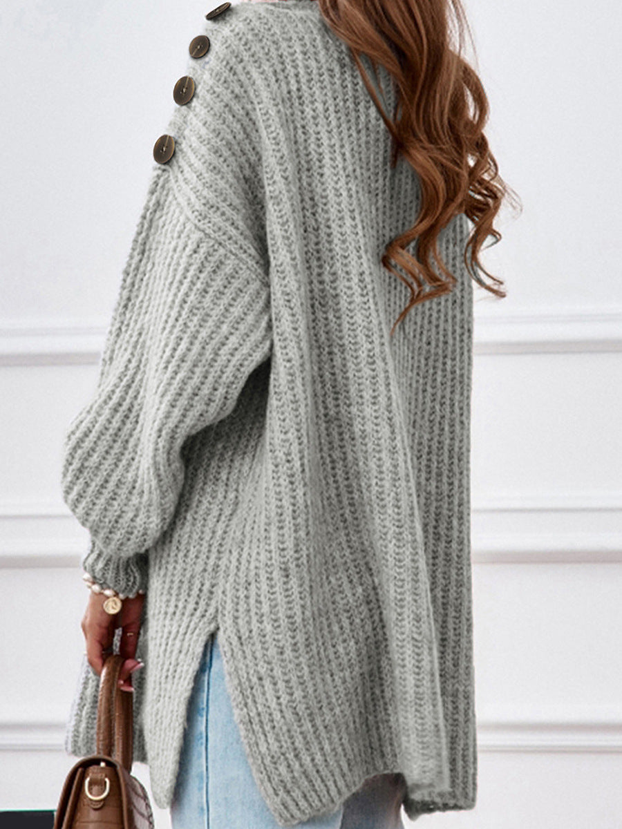 Person wearing a gray ribbed sweater with buttons, holding a brown handbag against a white background.