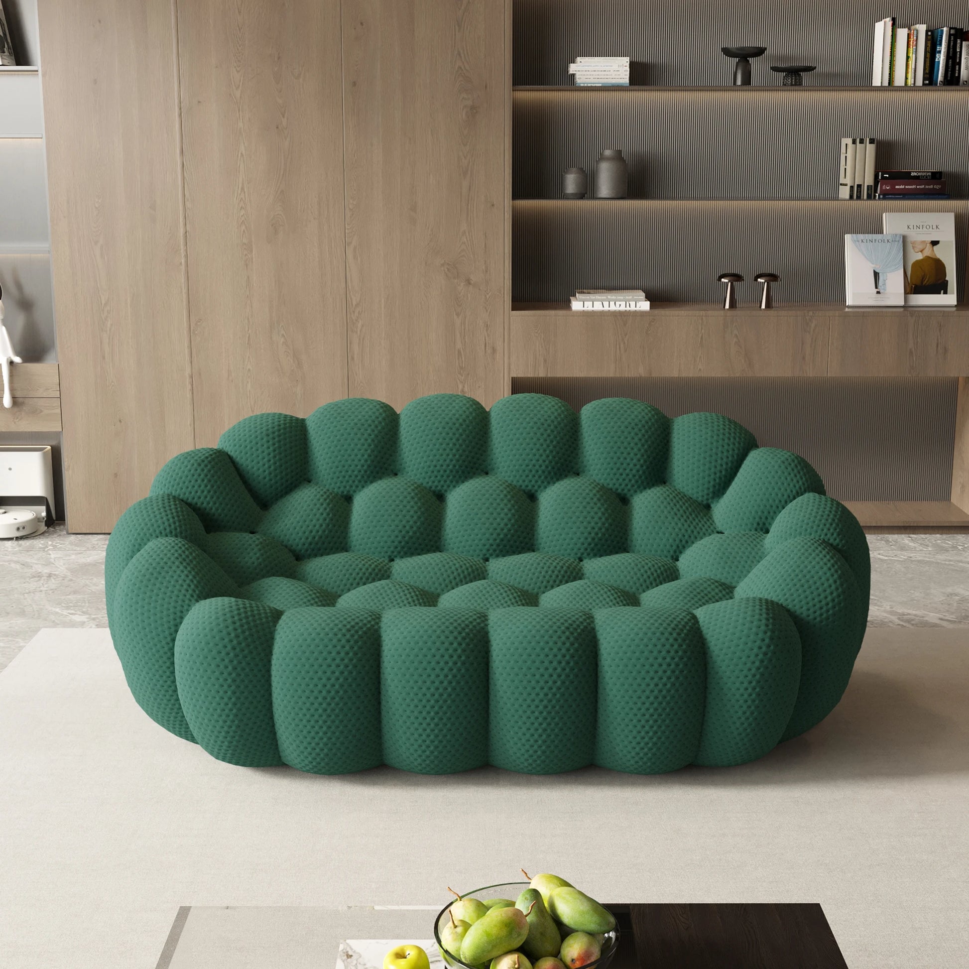Green textured sofa in a modern living room with a bookshelf and fruit bowl on a table.