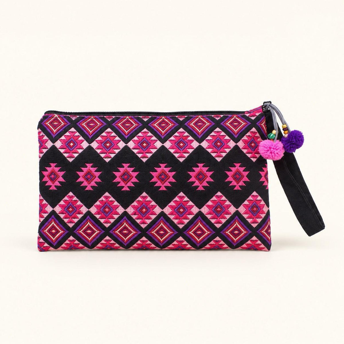 A rectangular zippered clutch bag with a vibrant geometric pattern in pink, magenta, and black, featuring a black wrist strap adorned with two purple pom-poms and a small gold charm.