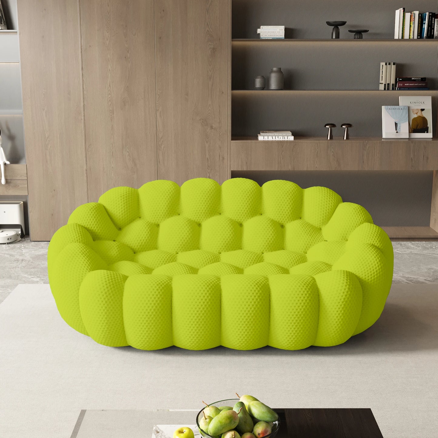 Green textured sofa in a modern living room with a bookshelf and fruit on a table.