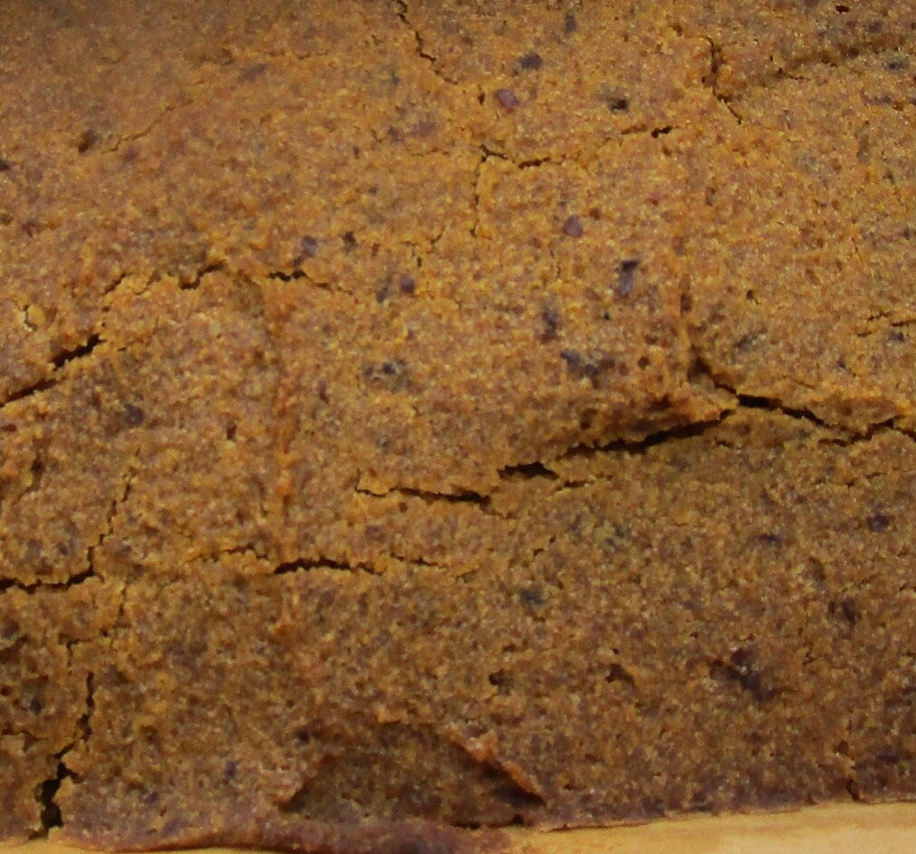 Loaf of pumpkin bread in a wooden loaf pan with bee-themed decorations in the background.