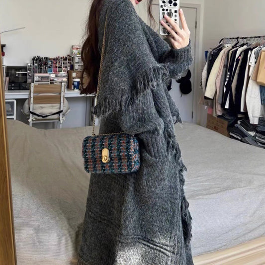 Person wearing a long gray coat holding a patterned handbag in a room with clothing racks and shelves.