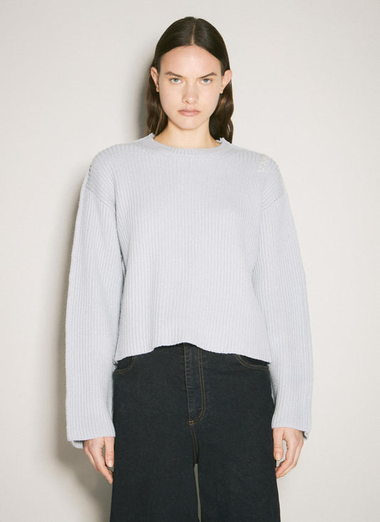 A person wearing a light gray Marni crewneck wool sweater paired with dark trousers, posed against a minimalist, neutral background.