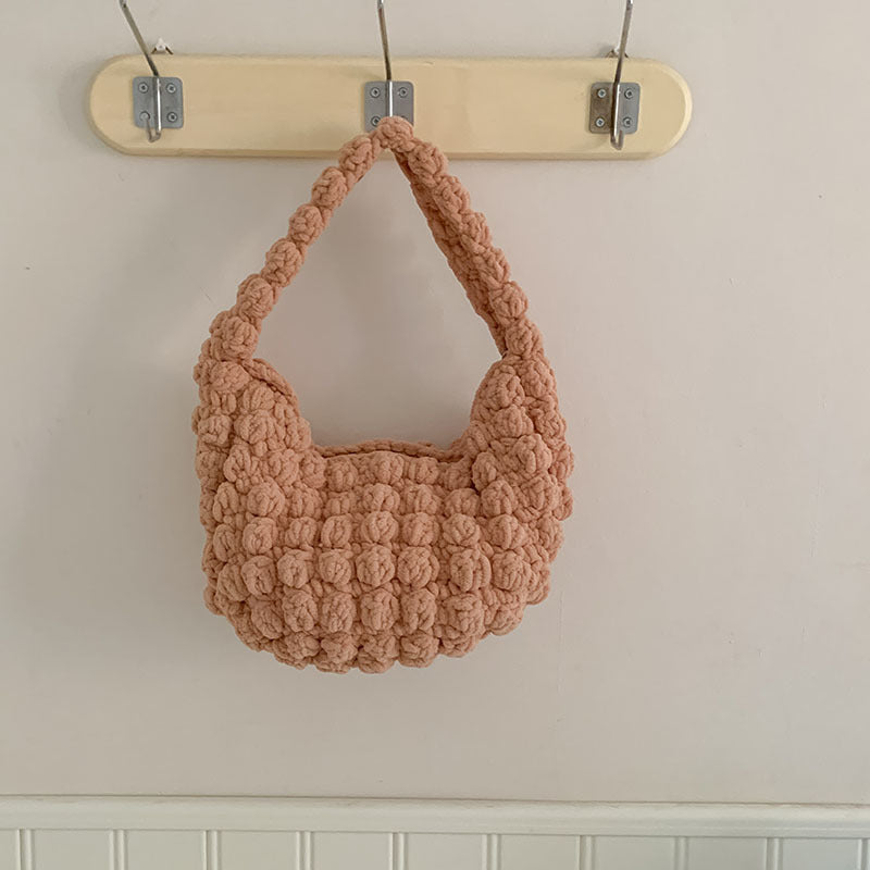Crocheted handbag hanging on a hook against a neutral wall.