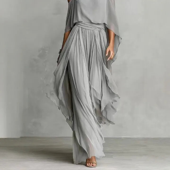 Flowing light gray chiffon two-piece co-ord set featuring an asymmetrical camisole top and wide-leg pants, modeled in an elegant resort-style outfit against a neutral background.