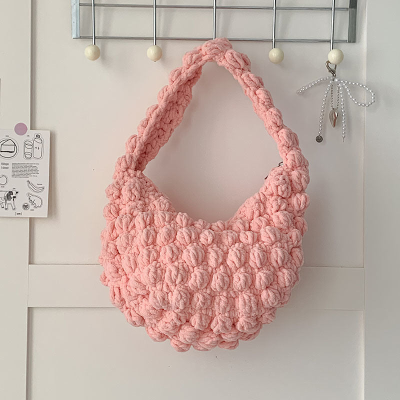 Pink knitted bag hanging on a hook against a white wall.