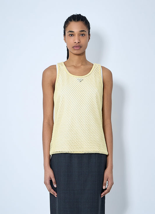 A model wearing a pale yellow open-knit sleeveless top and dark gray wide-leg trousers, standing against a light blue-gray studio background.