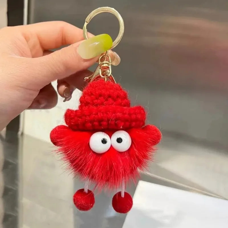 Red plush keychain with googly eyes held by a hand against a neutral background
