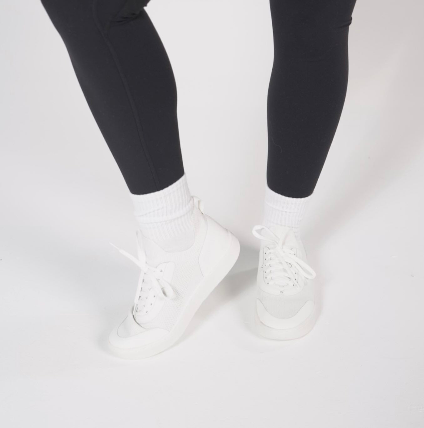 White sneakers worn with black leggings on a light gray background