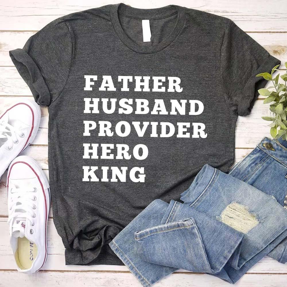 Gray t-shirt with 'Father Husband Provider Hero King' text, paired with jeans and sneakers on a wooden surface.