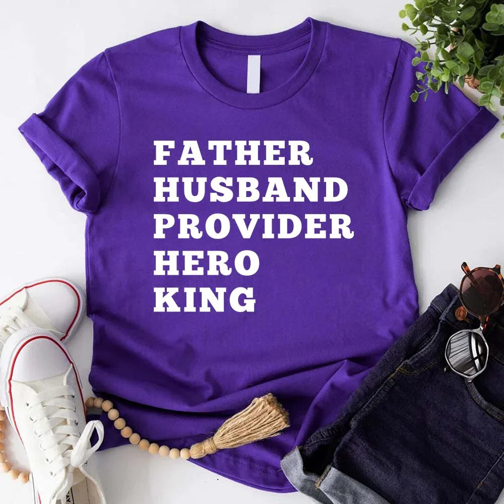 Purple t-shirt with text 'FATHER HUSBAND PROVIDER HERO KING' on a white surface with accessories.
