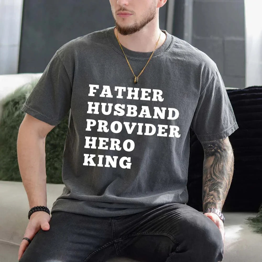 Man wearing a t-shirt with text 'FATHER HUSBAND PROVIDER HERO KING' in a casual setting.