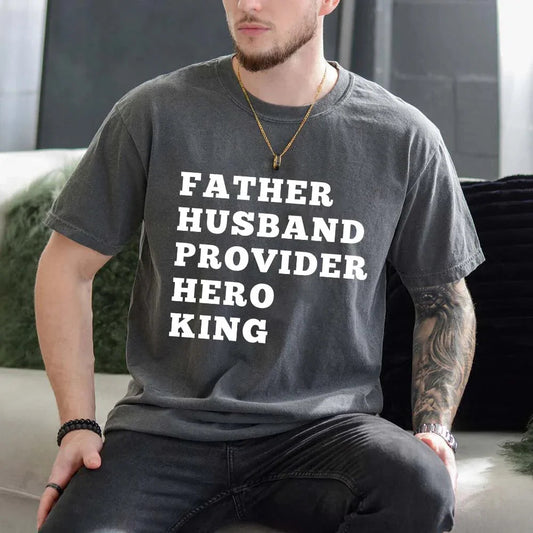 Man wearing a t-shirt with text 'FATHER HUSBAND PROVIDER HERO KING' in a casual setting.