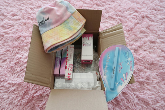Open box containing various items including a colorful towel, boxes of makeup, and a blue and pink product. - MYSTERY BOX SPOILED LIPS COSMETICS